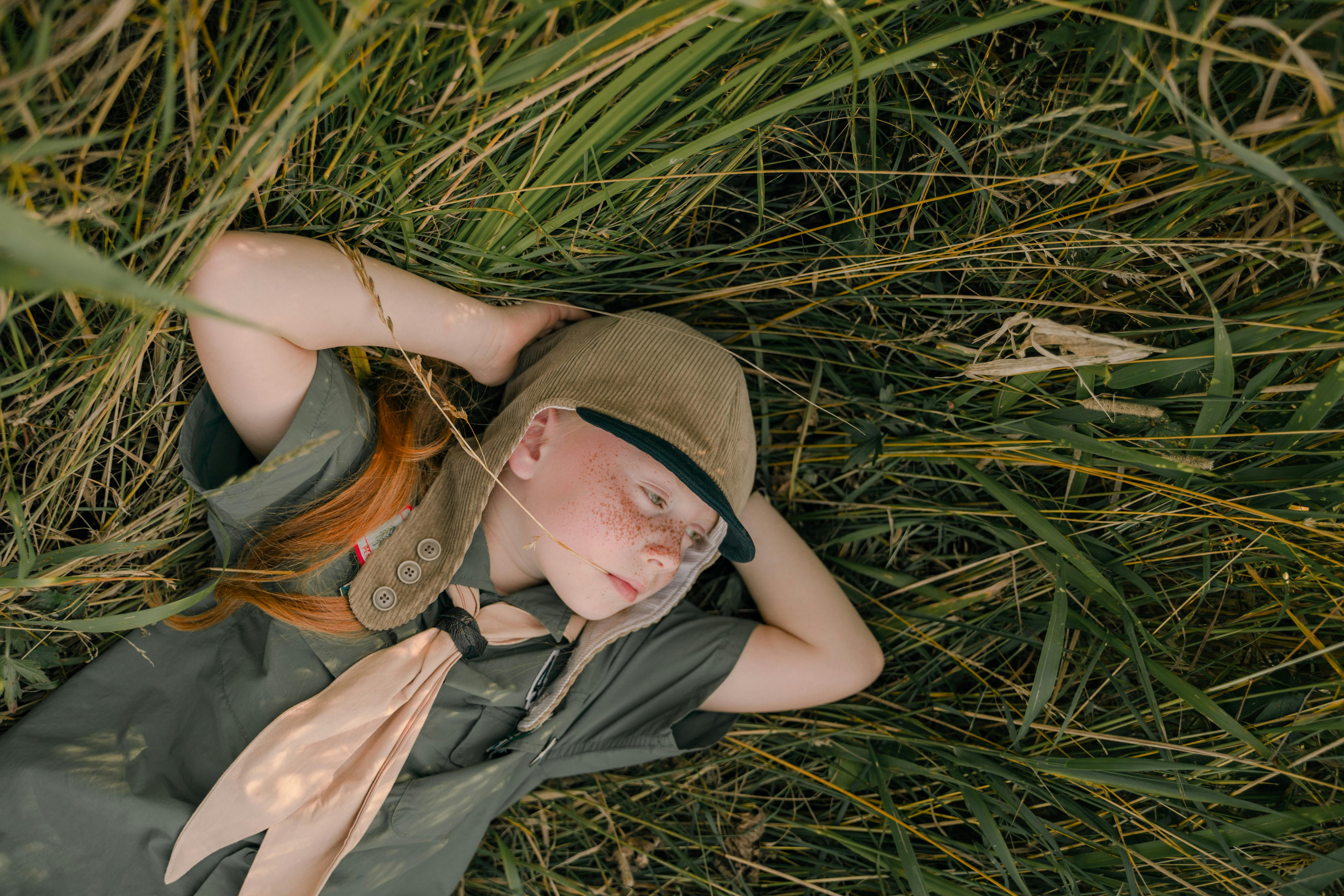 A young girl scout with freckles relaxes on grass on a sunny day, capturing tranquility and nature.