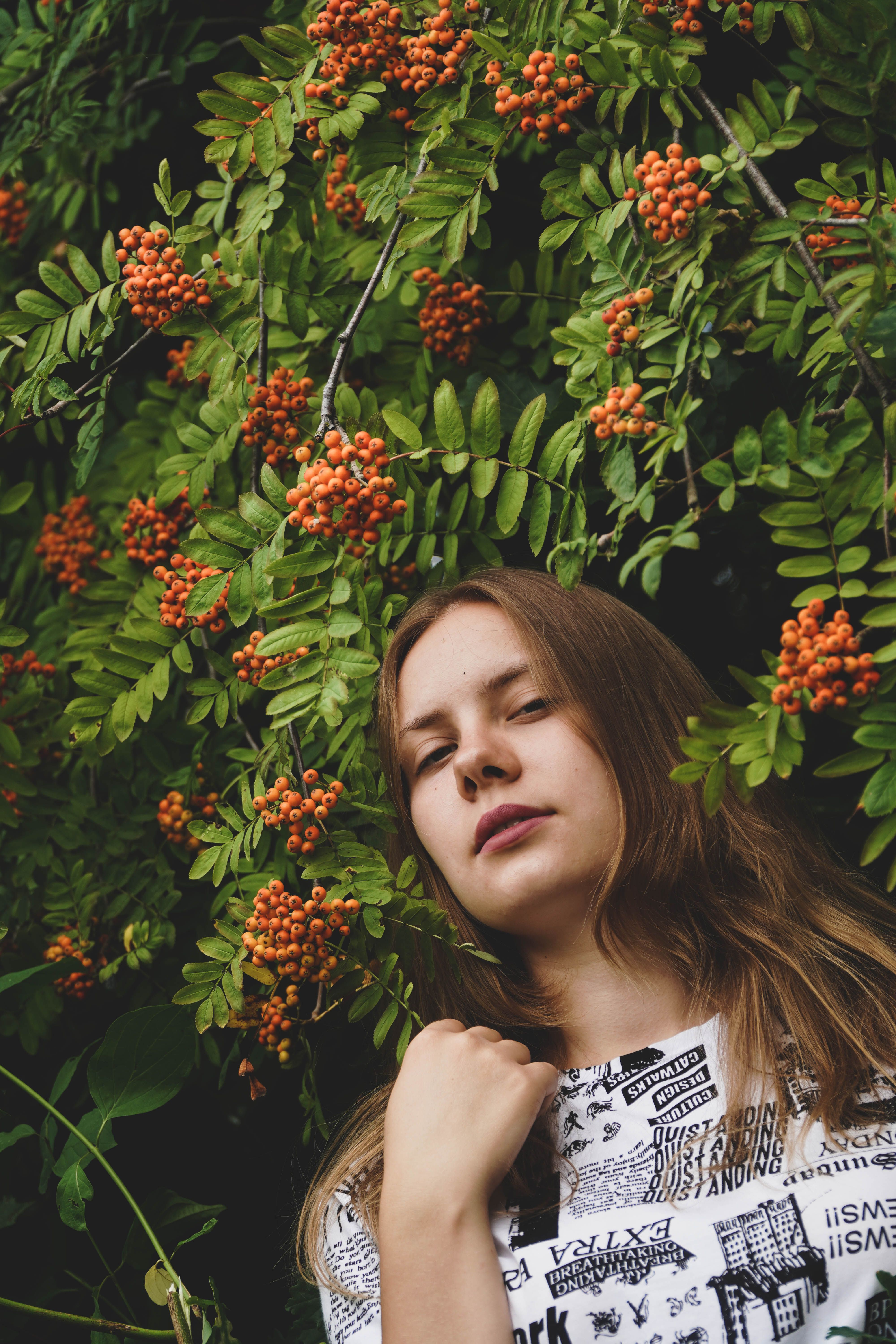 A young woman posing amidst lush green foliage and vibrant orange rowanberries.