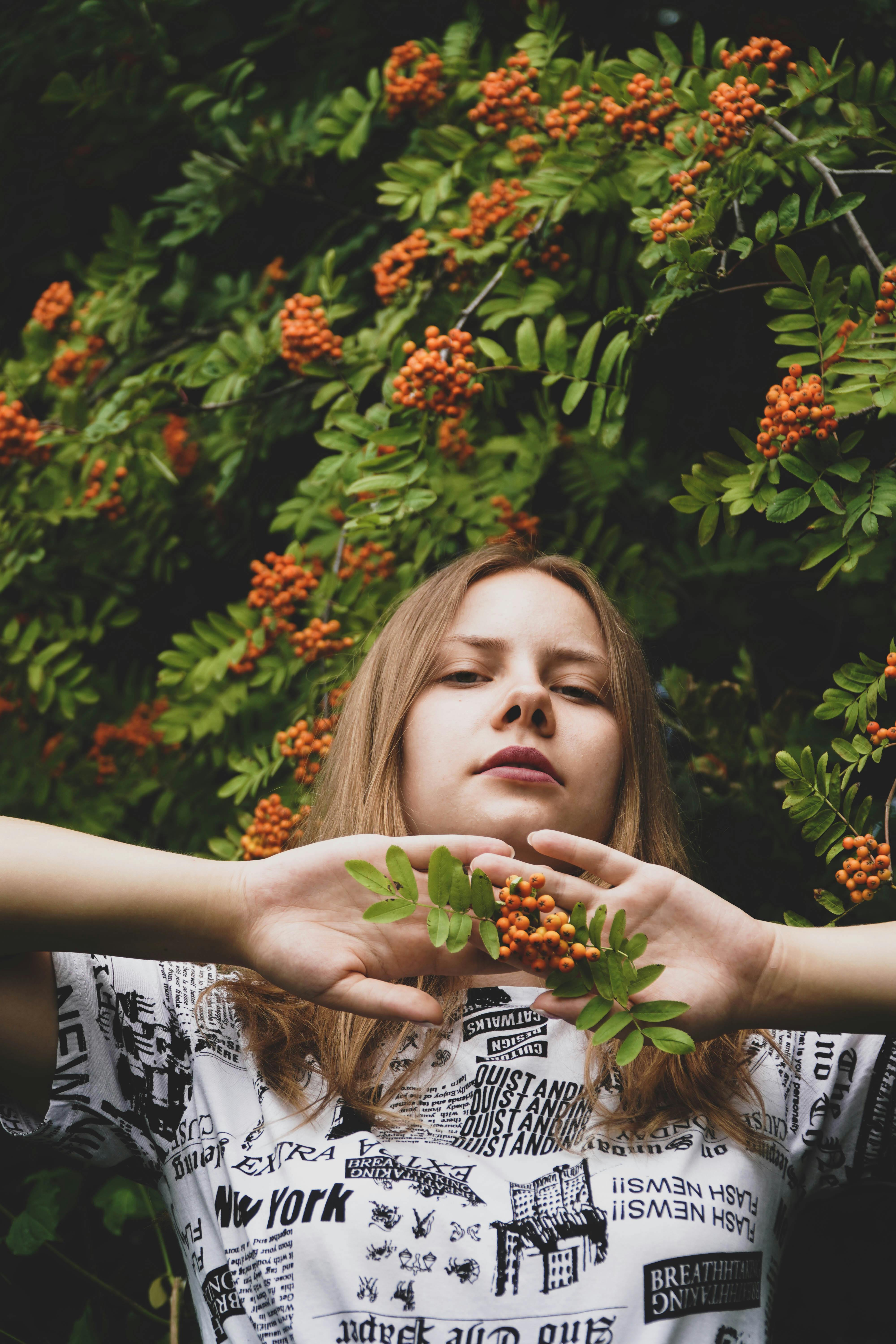 A young woman with blonde hair stands in a verdant garden holding vibrant red berries.