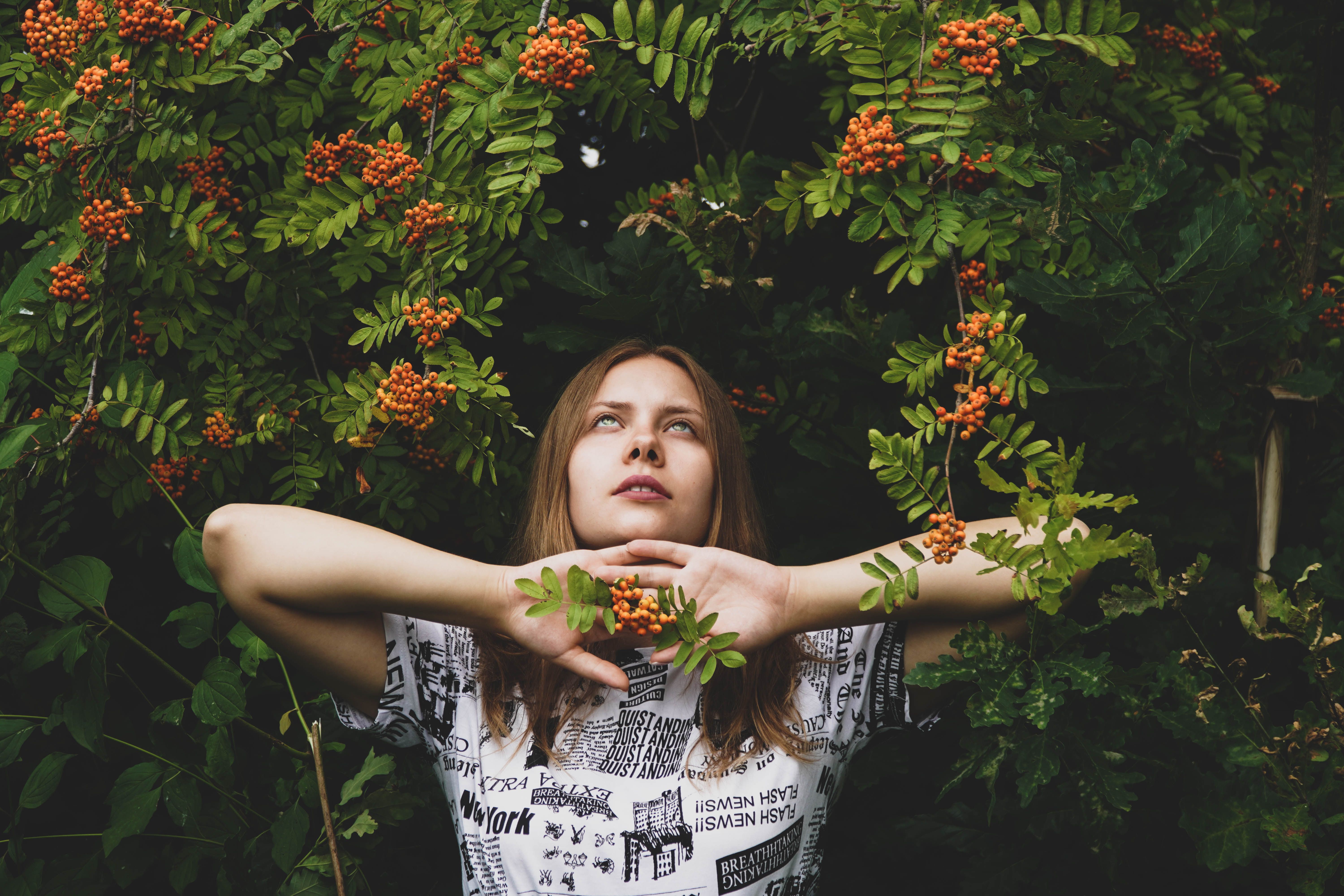 Young woman poses amidst lush foliage and vibrant mountain ash berries outdoors.