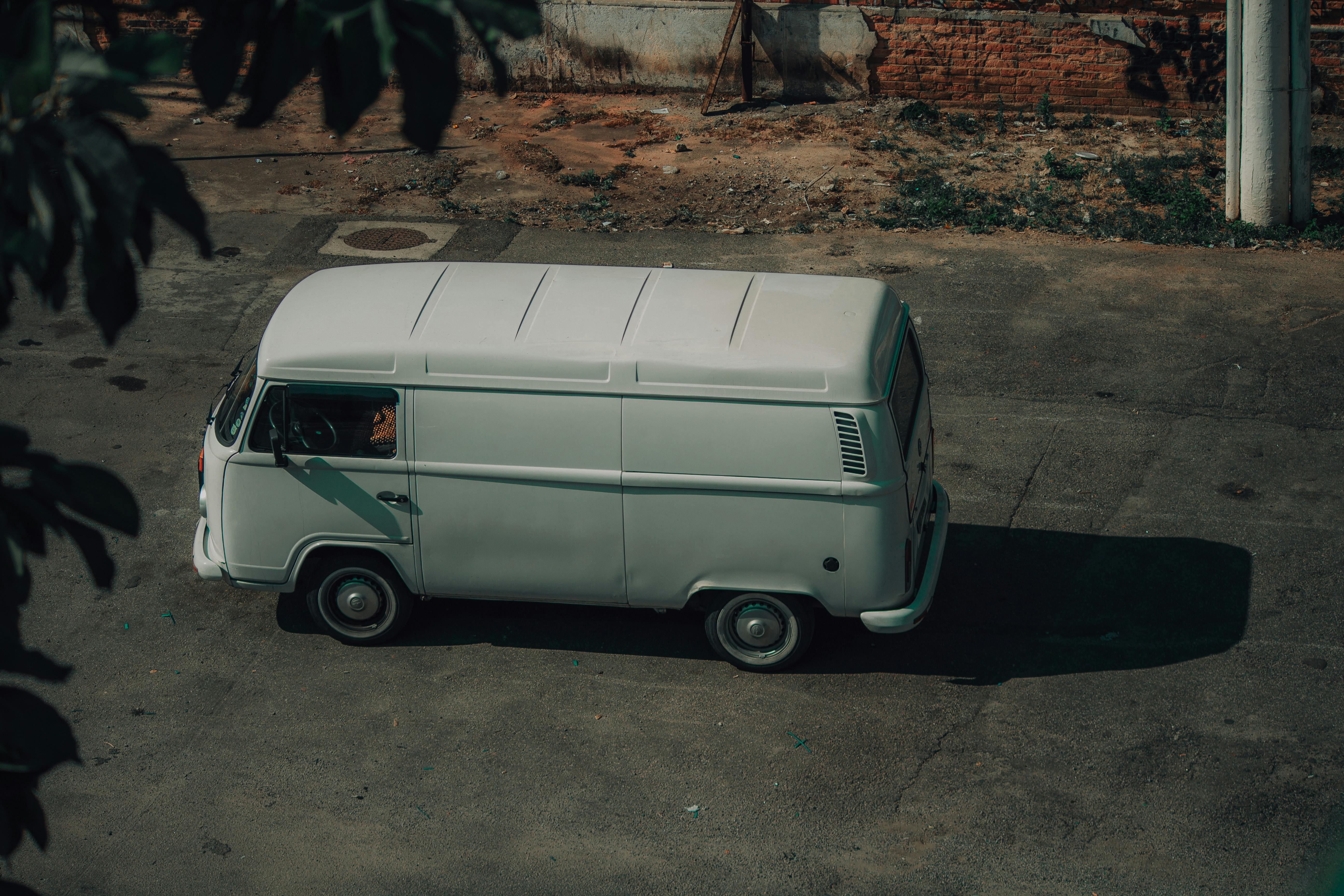 Free A classic white van parked on a street, surrounded by urban elements, captured in natural light. Stock Photo