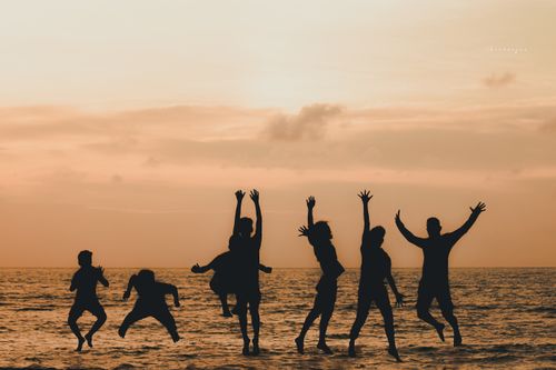 Free Silhouettes of people jumping joyfully at the beach during sunset with an orange sky. Stock Photo