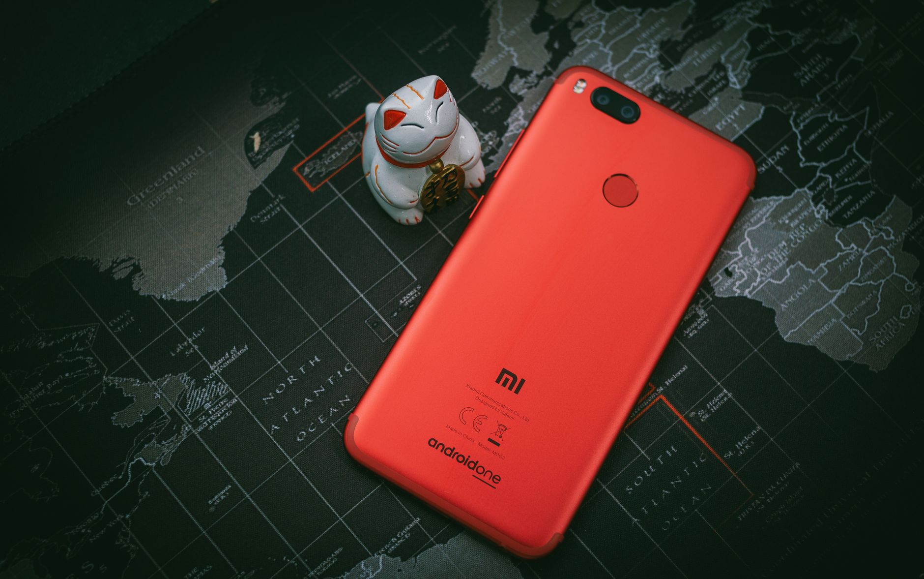 國外社群收不到簡訊怎麼辦?手機通訊備案5步解決 Red smartphone placed on a world map background with a cat figurine. Focus on modern technology.