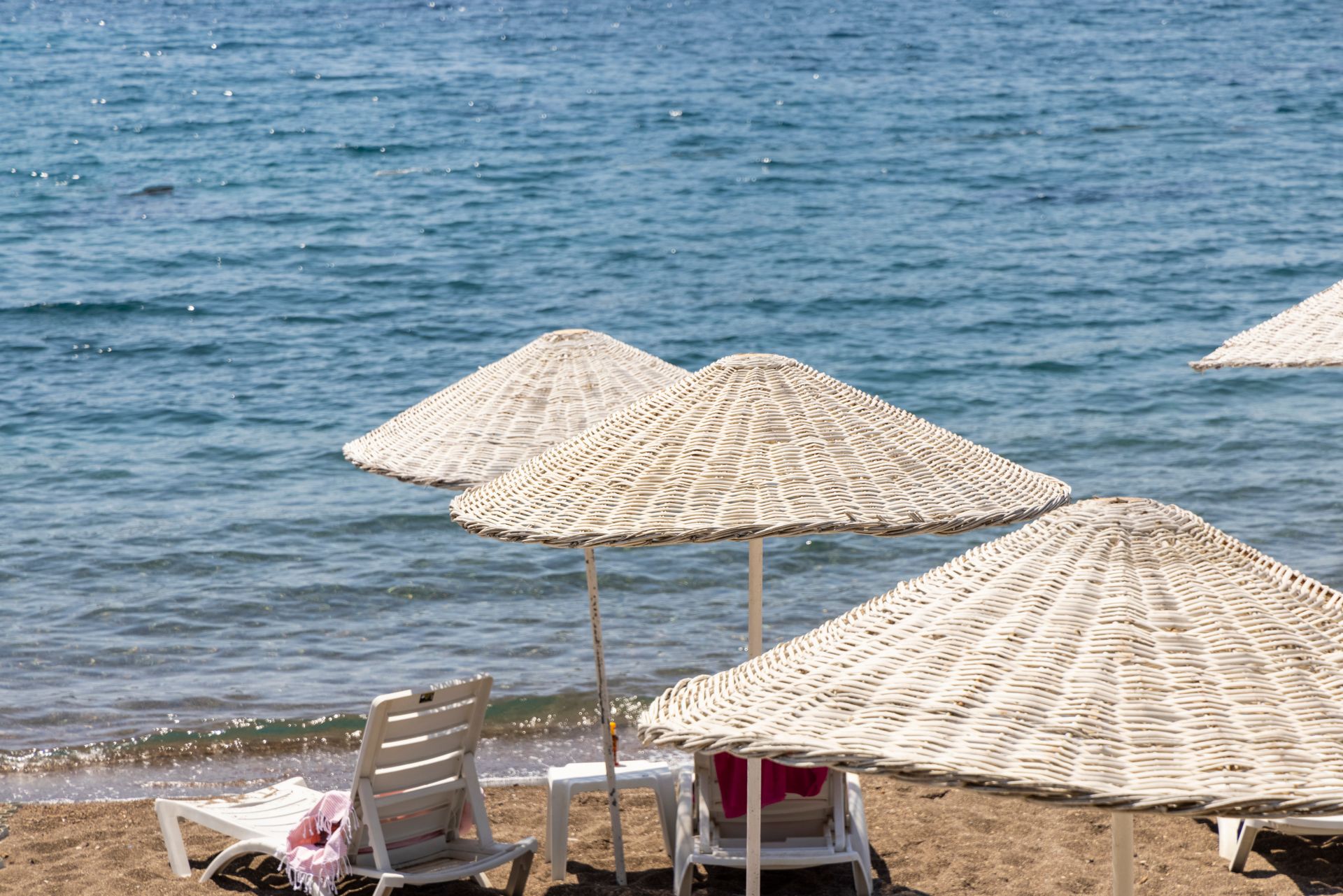 Tranquil beach scene featuring wicker umbrellas and sun loungers by the shore.
