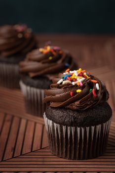 Three chocolate cupcakes with rich frosting and colorful sprinkles.