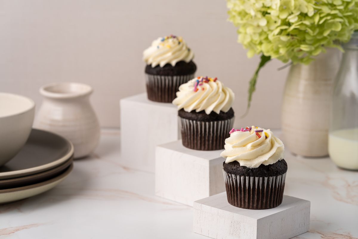 Three chocolate cupcakes with swirled buttercream and sprinkles on white risers. Photo by Skyler Ewing on Pexels.