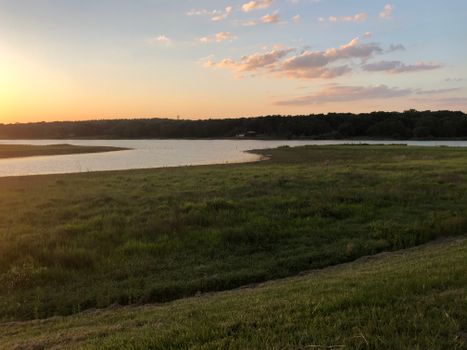 Peaceful sunset over a calm lake with lush green grass and orange sky.
