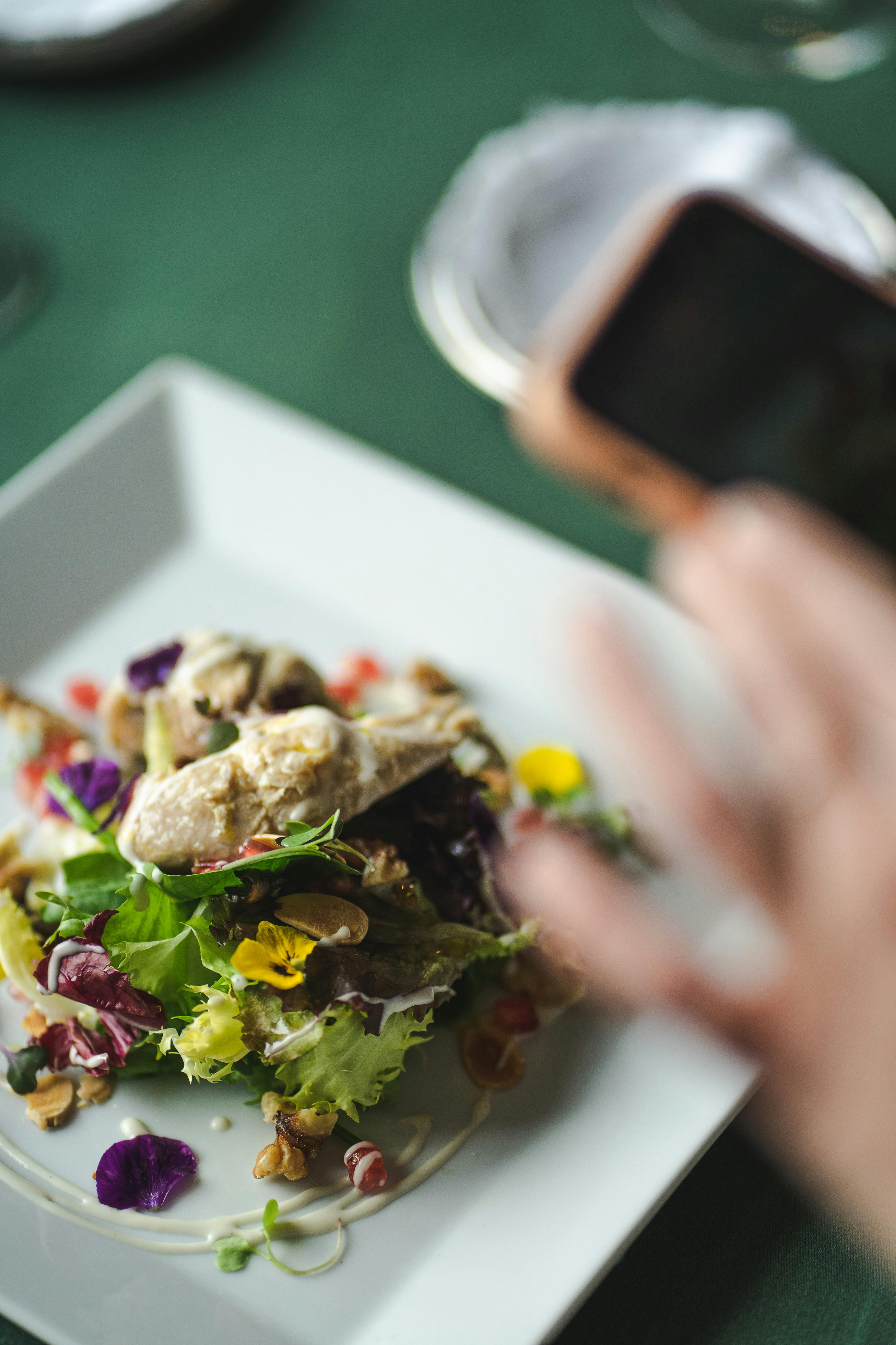 Colorful gourmet salad with edible flowers, being photographed on a green tablecloth.
