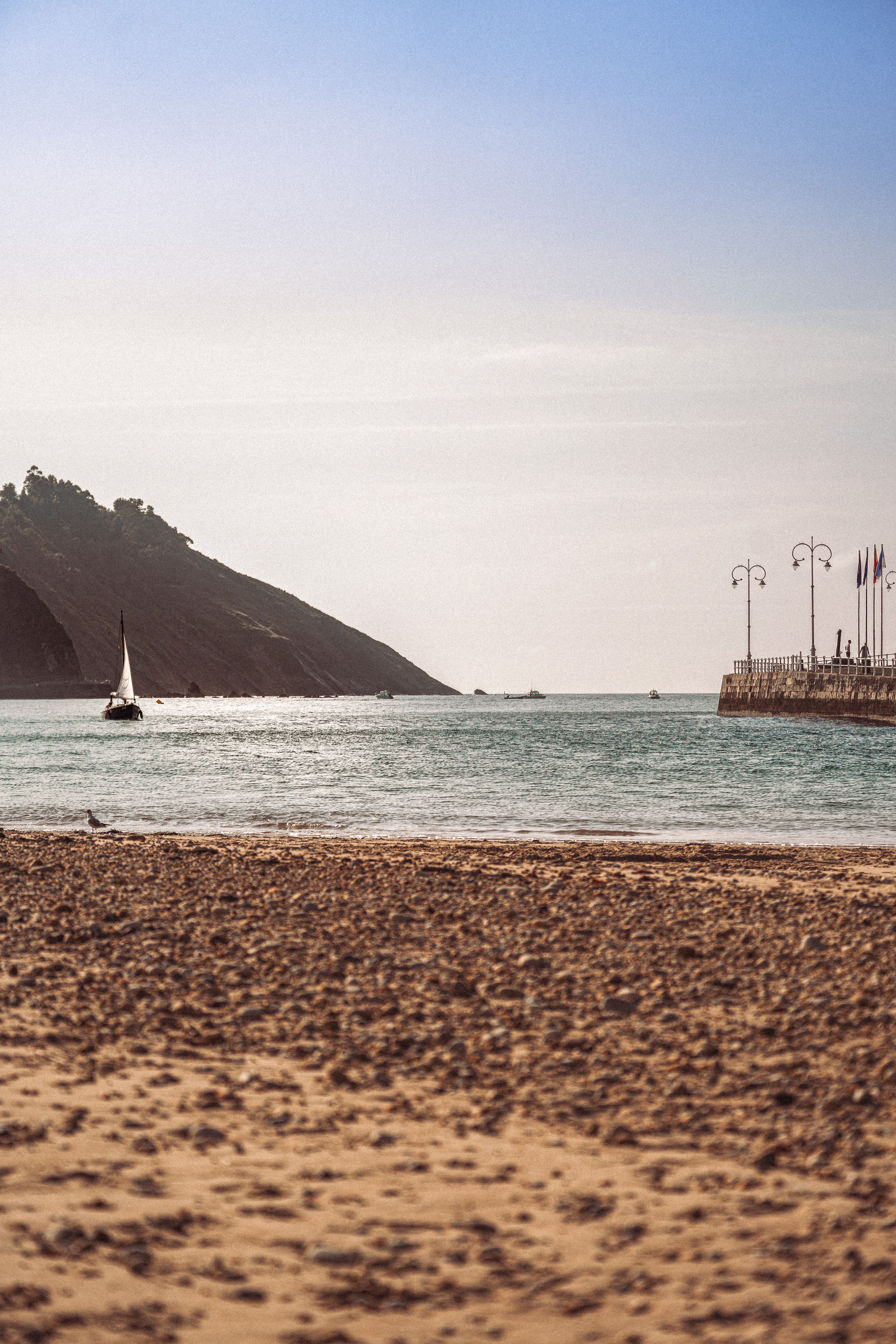 Tranquil beach scene with a sailboat offshore and a view of the seaside promenade.