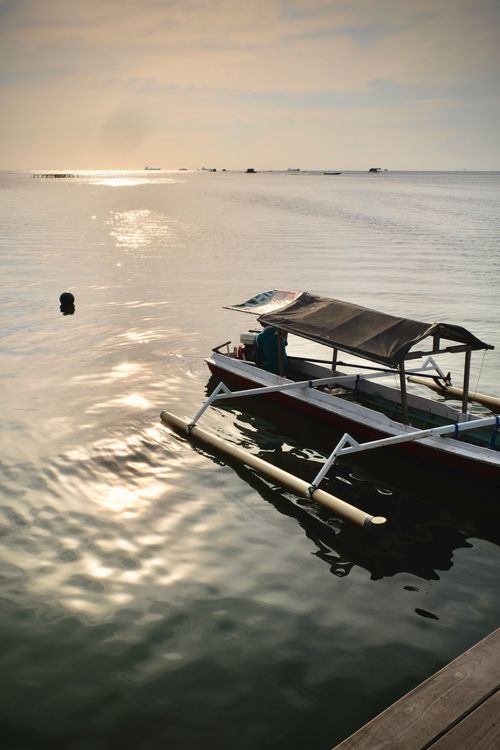 Free A traditional outrigger boat sits calmly on the sea with a serene sunset horizon in the background. Stock Photo