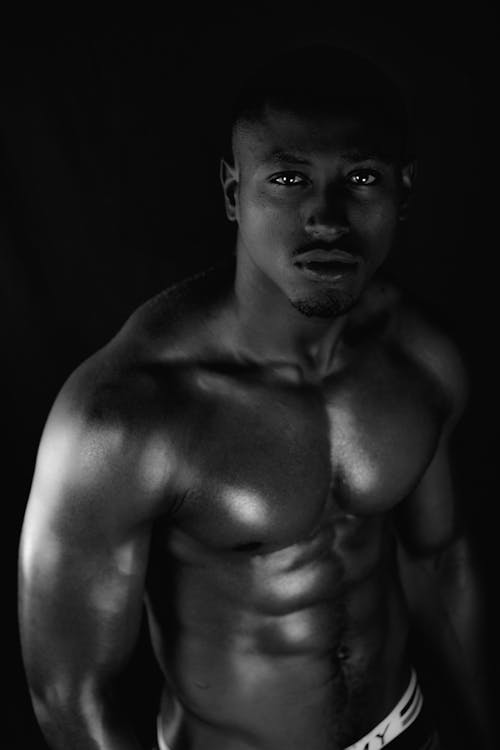 Grayscale Photo of a Topless Brawny Man Looking at the Camera