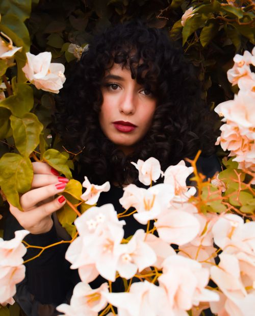 Free Elegant portrait of a woman with curly hair surrounded by blooming white flowers. Stock Photo