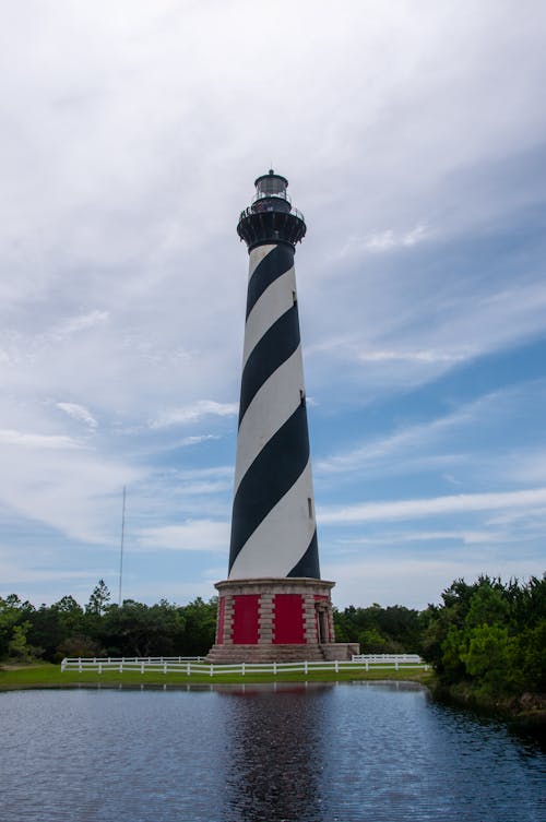 Free Striped Lighthouse Near Water Under the Sky Stock Photo