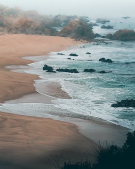 A breathtaking view of a coastal landscape with waves crashing against the rocks and mist enveloping the scene.