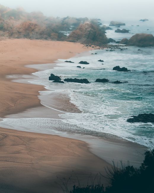 A breathtaking view of a coastal landscape with waves crashing against the rocks and mist enveloping the scene.