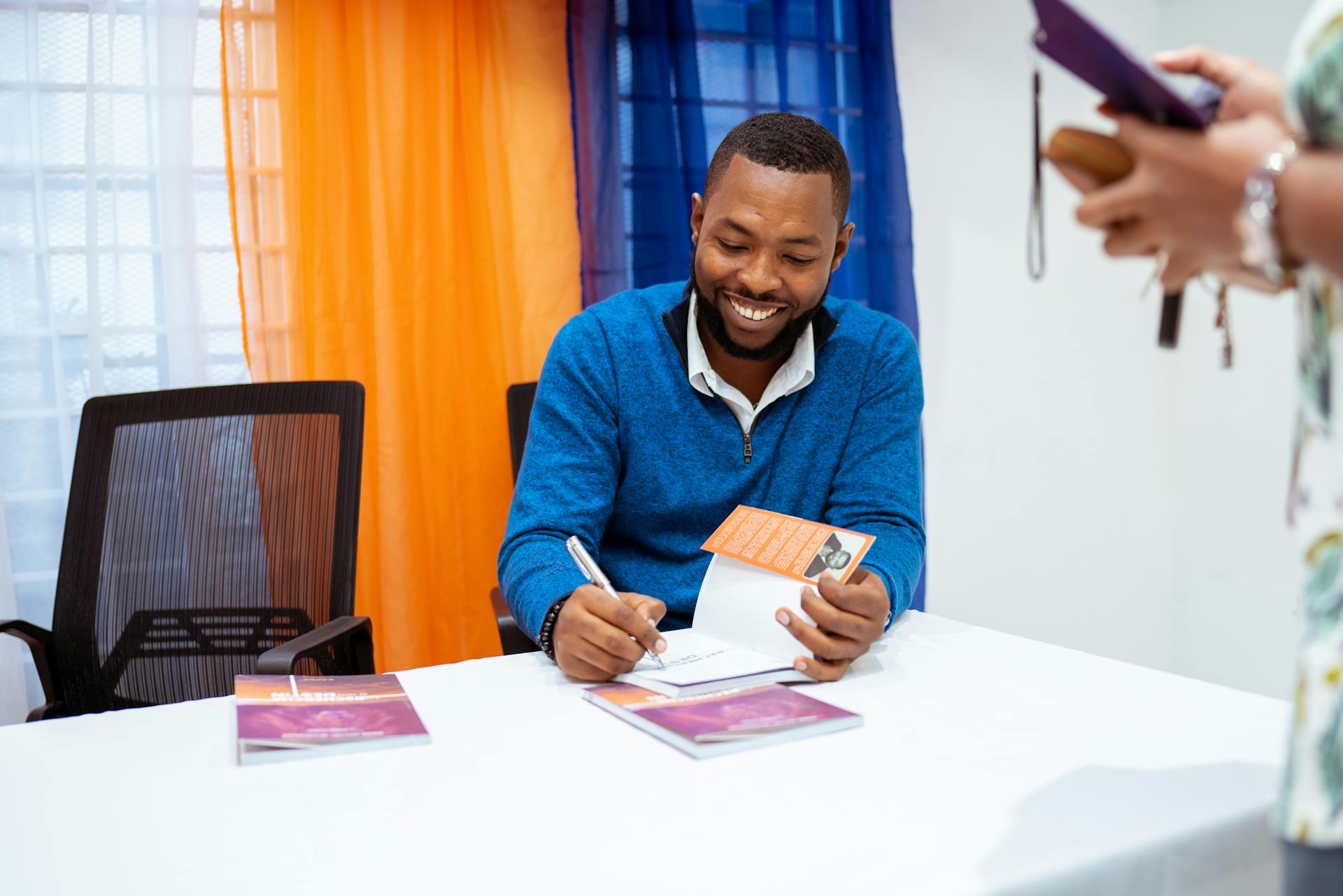 Smiling author signing books at a public event, engaging with readers.