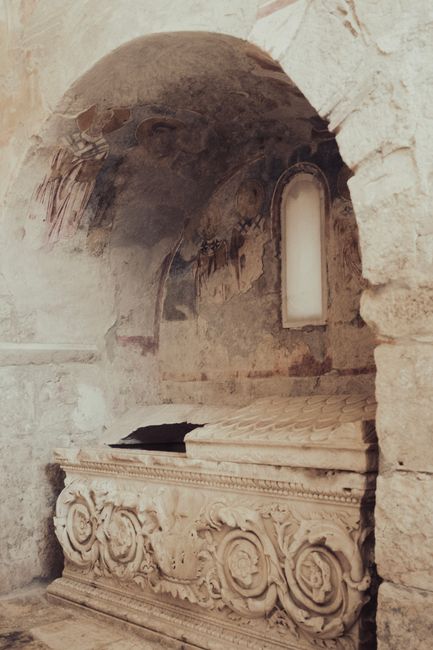 Fotomural Un sarcófago de piedra antiguo y ornamentado en un rincón arquitectónico histórico con arte desvanecido en las paredes.