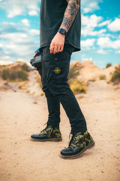 Person in Black Pants and Black Hiking Shoes Standing on Brown Sand
