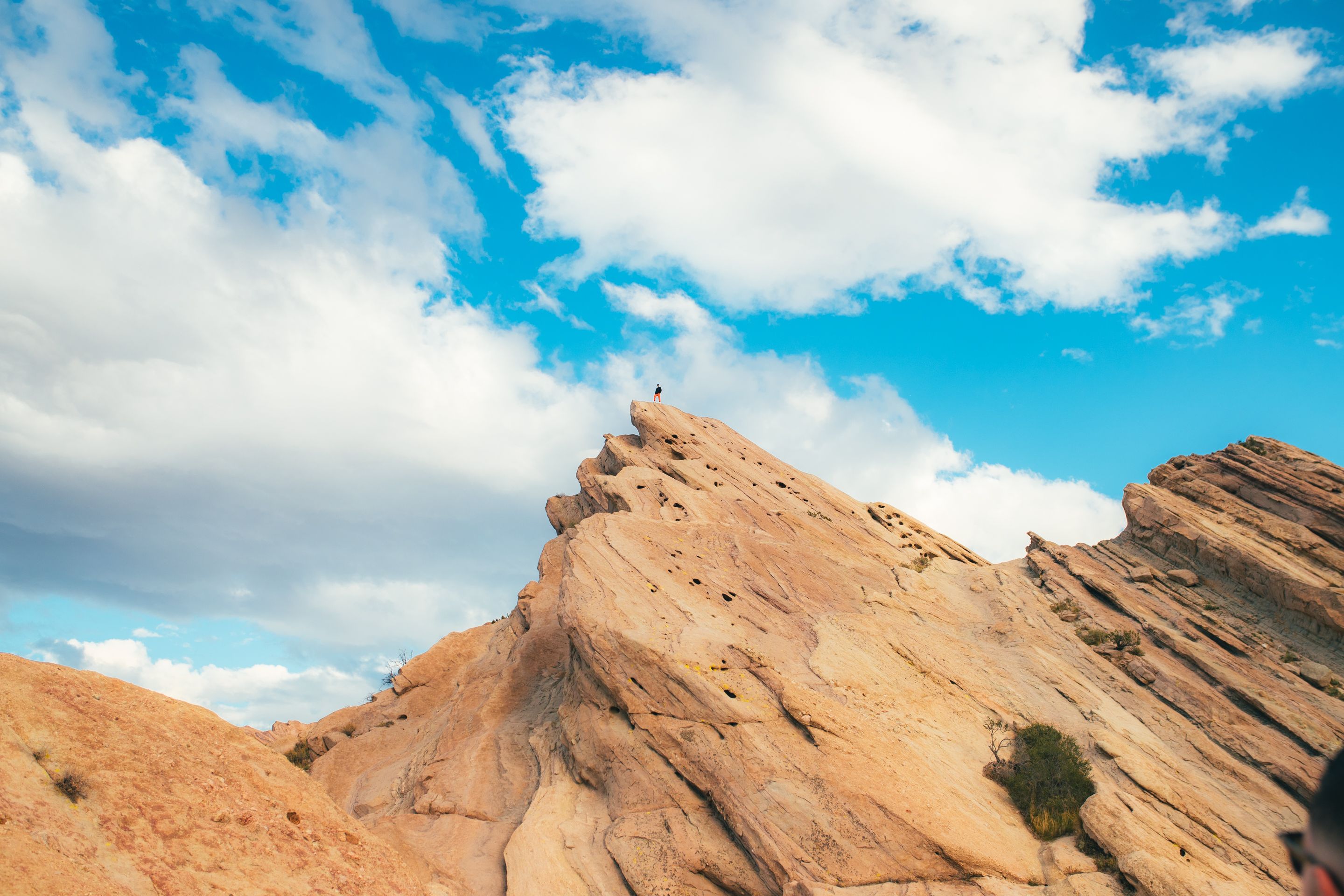 A person stands atop a rugged rock formation under a bright blue sky in Agua Dulce, California.