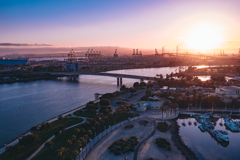 A serene sunset over a bustling harbor with bridges, cranes and tranquil waters.