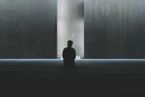 Free Silhouetted person sitting in a dark minimalist space with light reflection on walls. Stock Photo