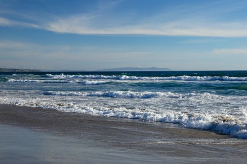 Free A tranquil scene of waves gently crashing onto Manhattan Beach under a bright blue sky. Stock Photo