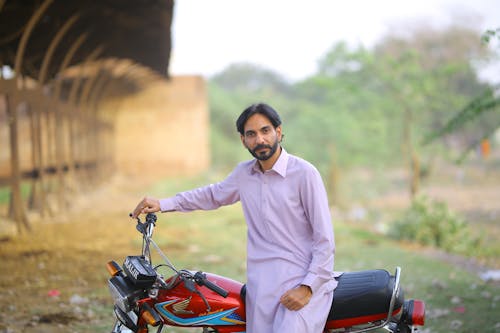 Man in Thobe Sitting on Red and Black Motorcycle