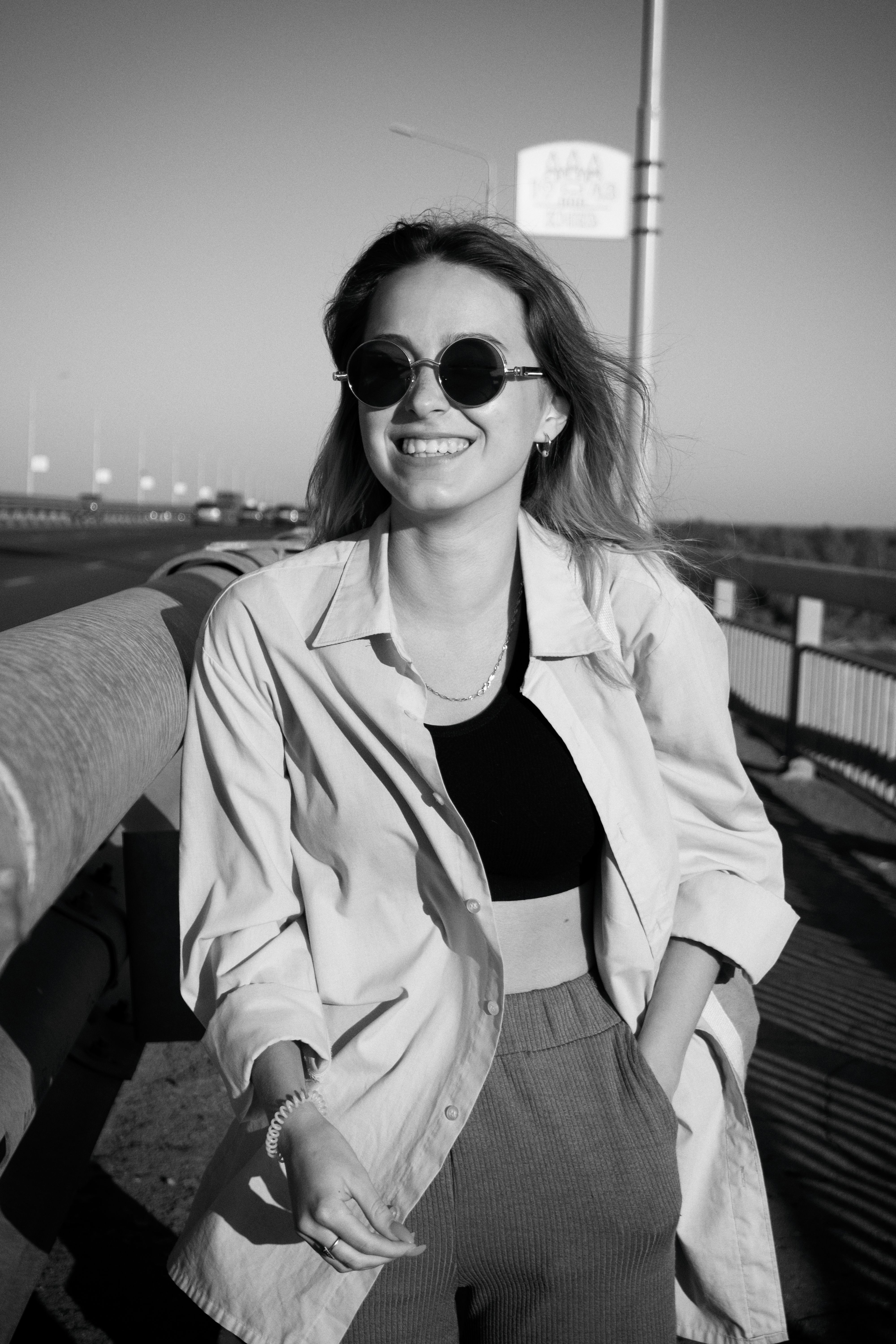 Black and white photo of a smiling woman wearing sunglasses outdoors.