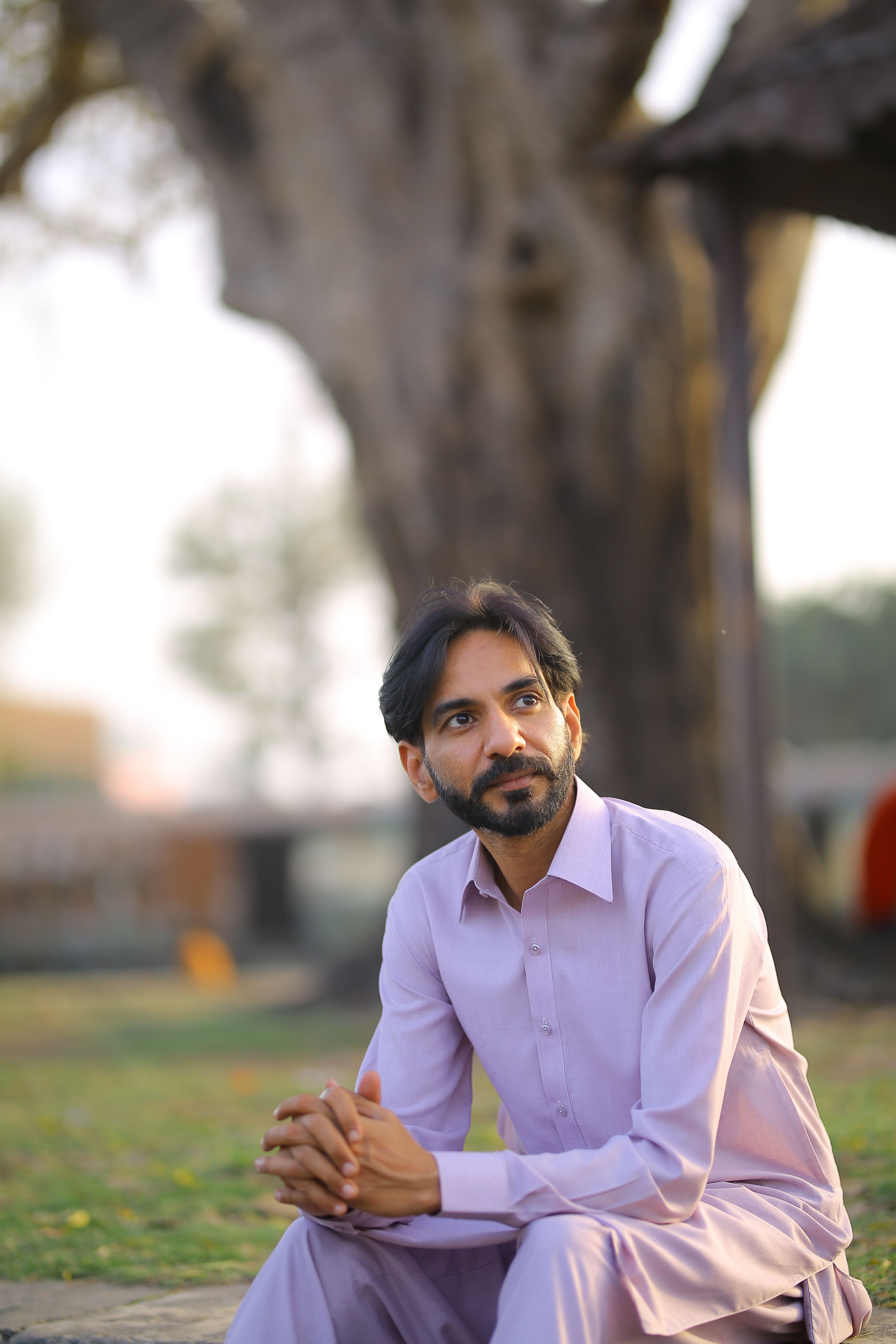 Contemplative man in a thobe sitting by a tree in a peaceful outdoor setting.