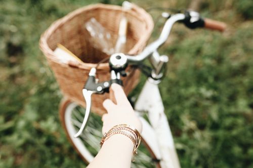 Free A hand grips the handlebar of a bike with a wicker basket in a grassy field. Stock Photo