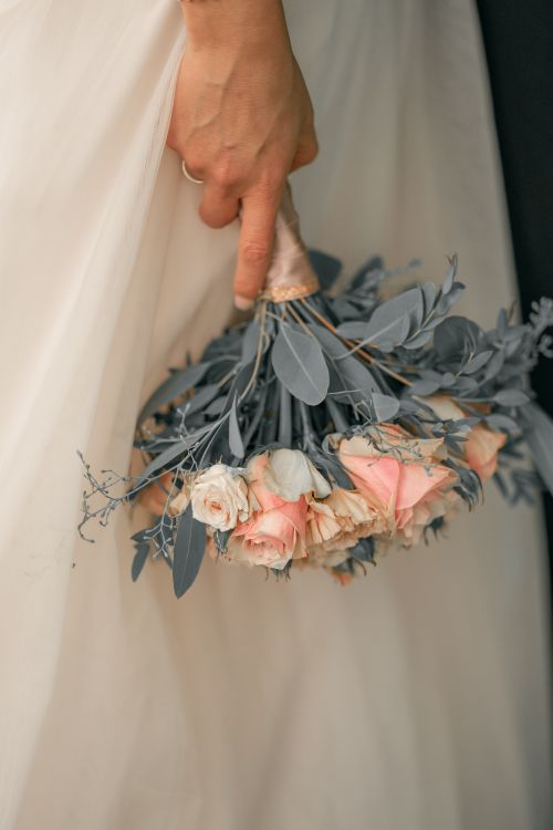 Free Close-up of a bride holding a bouquet of roses and leaves, showcasing elegant bridal details. Stock Photo