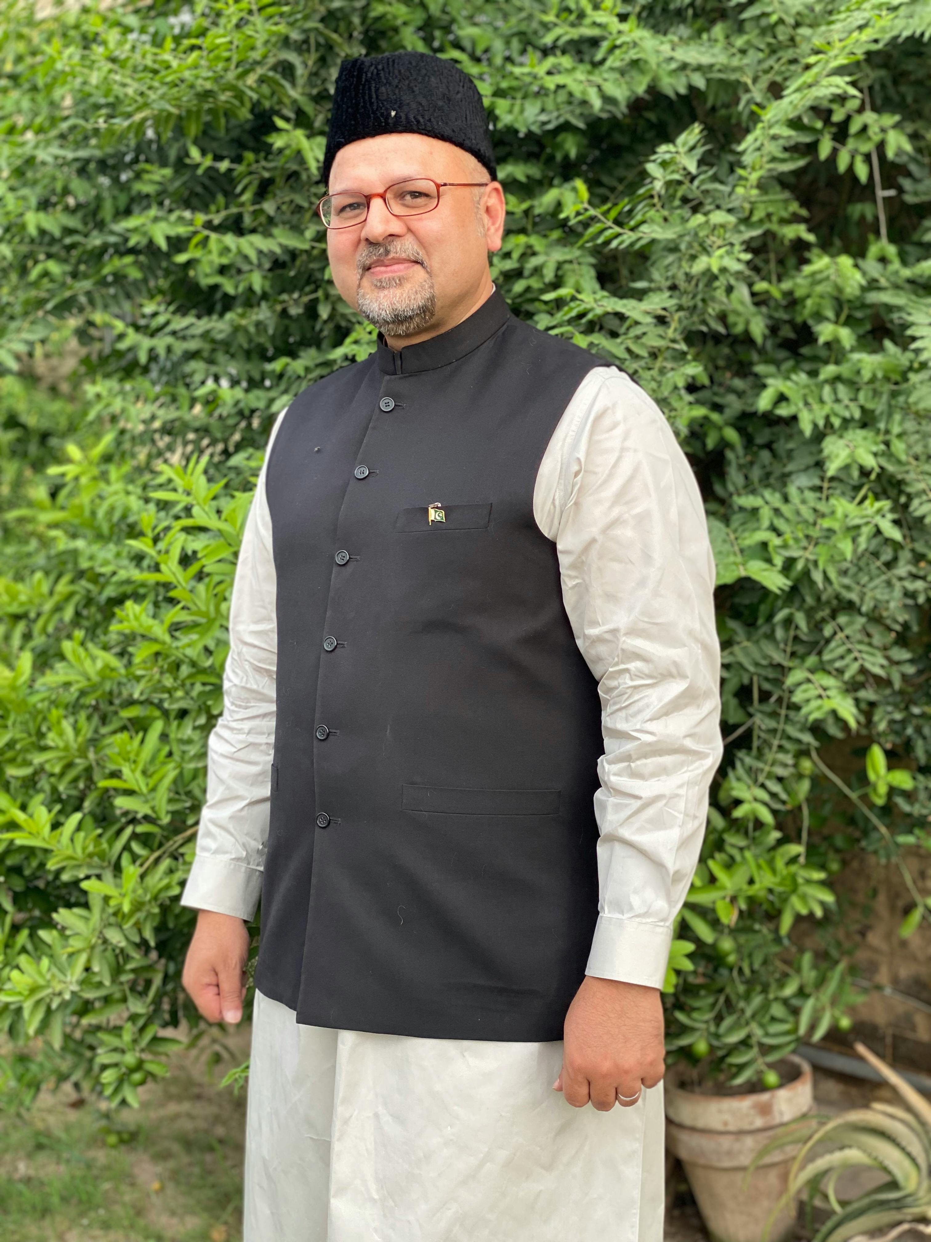 Portrait of a man wearing traditional clothing and a karakul hat outdoors in Lahore.