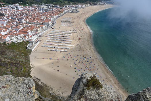 Stunning aerial view of Nazaré beach in Portugal with umbrellas and vibrant coastline, perfect for summer travel inspiration.