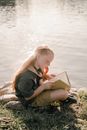 A Girl Reading a Book Near the Body of Water