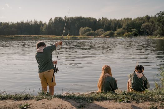 Three children fishing at a peaceful lake shore under clear skies.