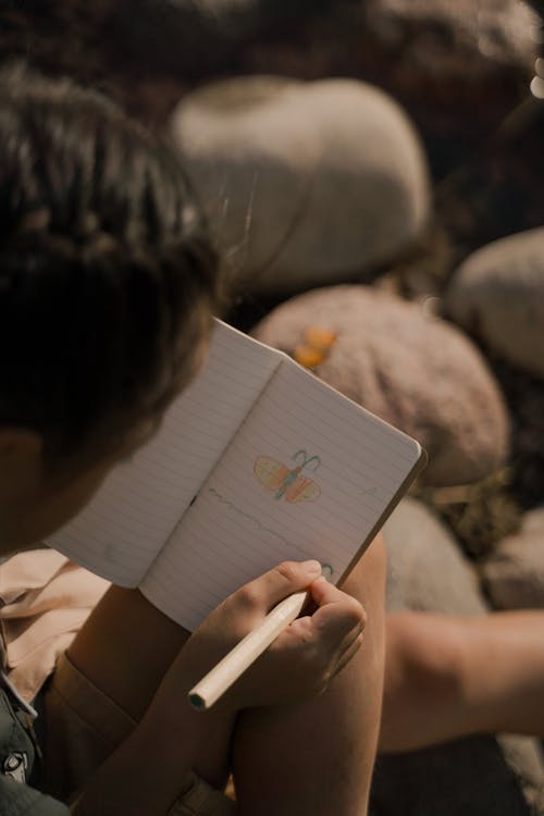 Person Holding a Colored Pencil and Notebook