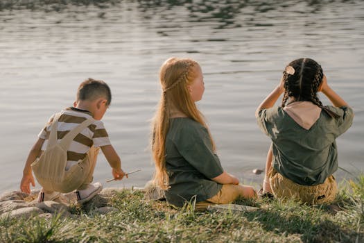 A group of children sits by the lake during summer, enjoying nature and camaraderie.