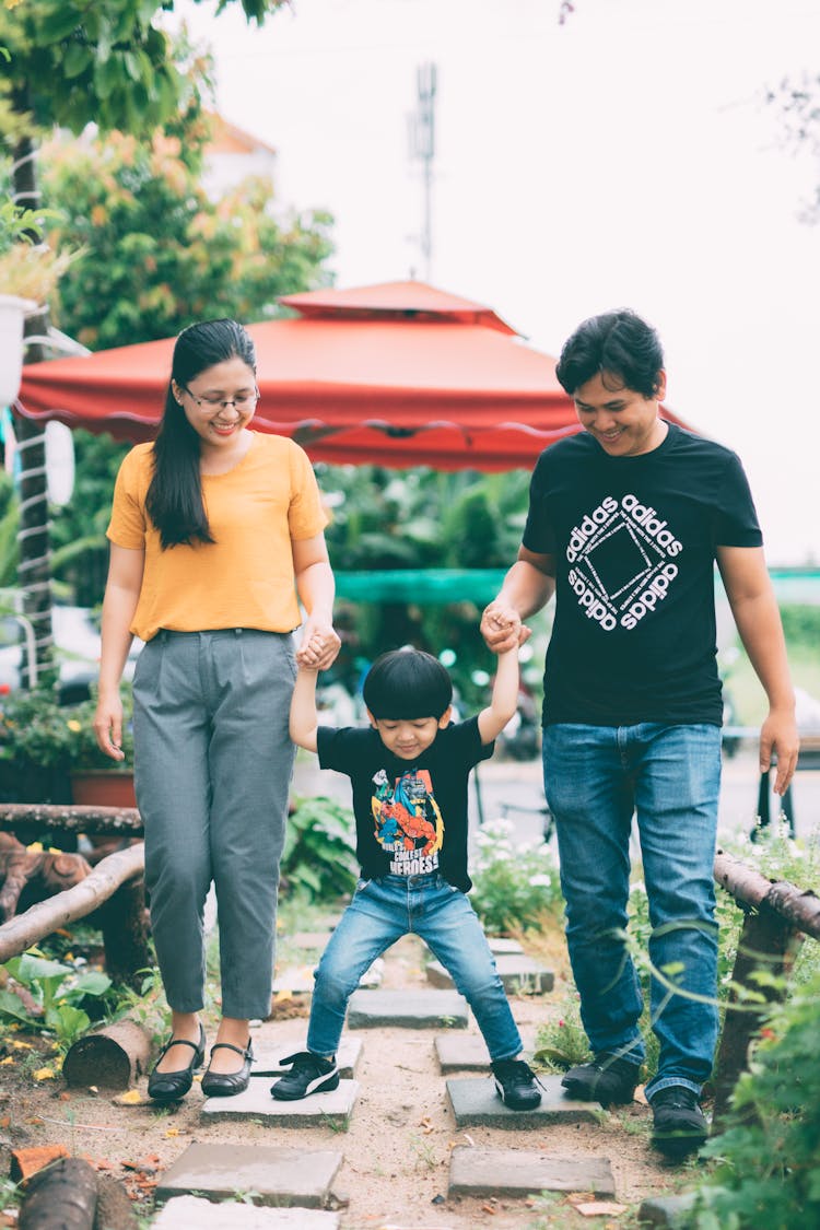 A Playful Child Holding Hands With His Parents