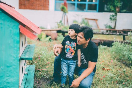 A father and son bonding by a playhouse in a lush garden setting.