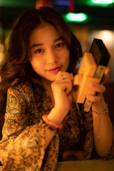 A young woman in a floral shirt holding a VHS tape, with a warm indoor setting.