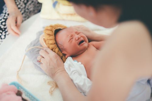 Free A crying newborn baby lying on a bed while being comforted by a parent, showcasing early life moments. Stock Photo