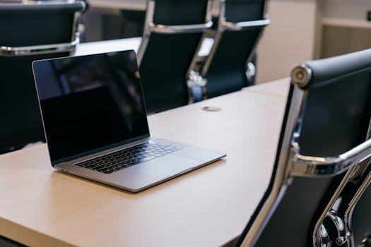 Open laptop on a wooden conference table with stylish black chairs in a modern office setting.