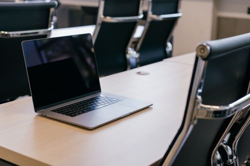 Free Open laptop on a wooden conference table with stylish black chairs in a modern office setting. Stock Photo