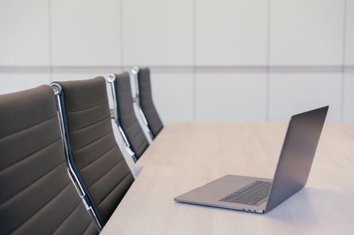 Free Minimalist office setup featuring a sleek laptop and stylish office chairs at a wooden table. Stock Photo