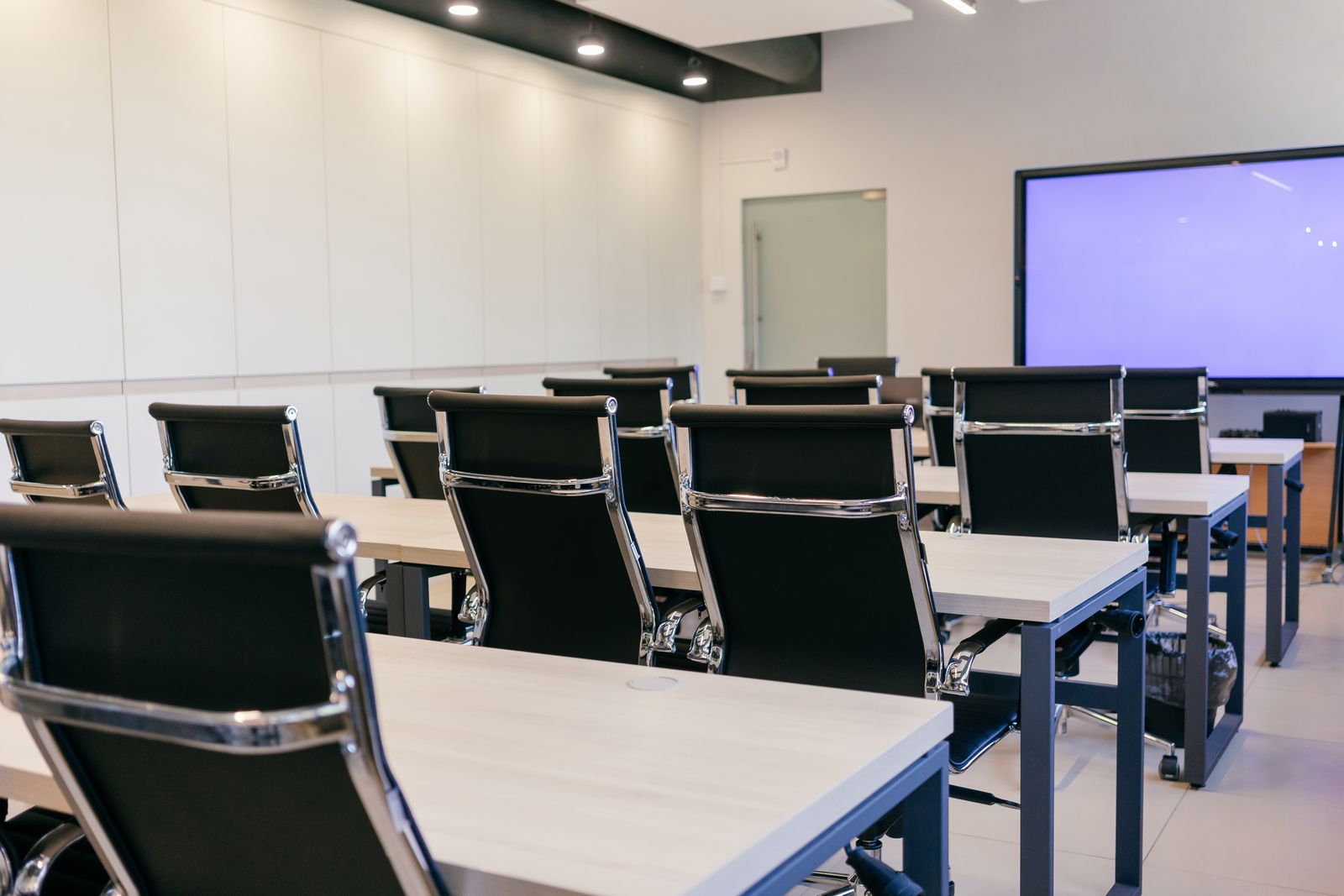 An empty modern corporate training room with rows of executive chairs and desks facing a large display, signalling the structured cohort environment in which TKH Global Group delivers TechAcademy programmes