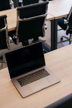 A sleek office setting featuring a laptop on a desk and modern black chairs.