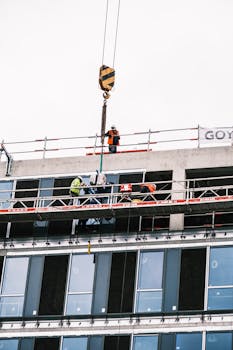 Construction workers on scaffolding at a high-rise building site with crane lifting materials.