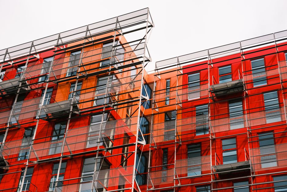 Contemporary architectural design featuring vibrant orange and red panels with glass windows and metal framework.