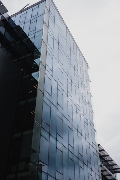 Free Vertical view of a modern glass building reflecting the cloudy sky, showcasing architectural design. Stock Photo