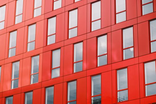 Free Close-up of a modern red building facade with reflective windows creating a geometric pattern. Stock Photo